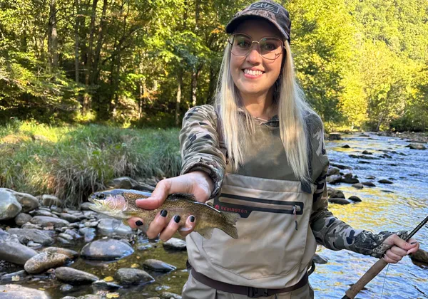 Gina fly fishing in waders on a river, holding a trout