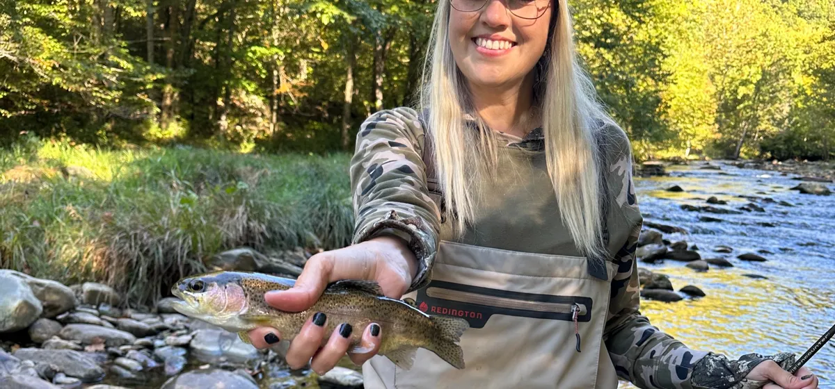 Gina fly fishing in waders, holding a trout