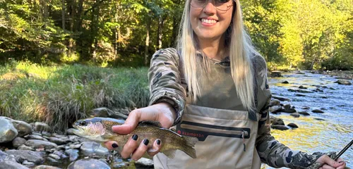 Gina fly fishing in waders, holding a trout